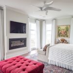 A bedroom with a fireplace and a red ottoman.