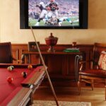 A pool table in the middle of a room with a television on.