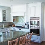 A kitchen with white cabinets and wooden chairs.