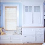 A white cabinet and window seat in the corner of a room.