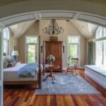 A bedroom with hard wood floors and a large arched window.