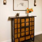 A cabinet with drawers and a vase of flowers on the wall.