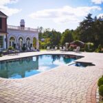 A large pool with chairs around it and a house in the background.