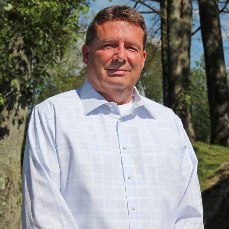 A man in white shirt standing next to trees.