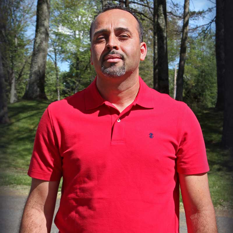 A man in a red shirt standing on the side of a road.