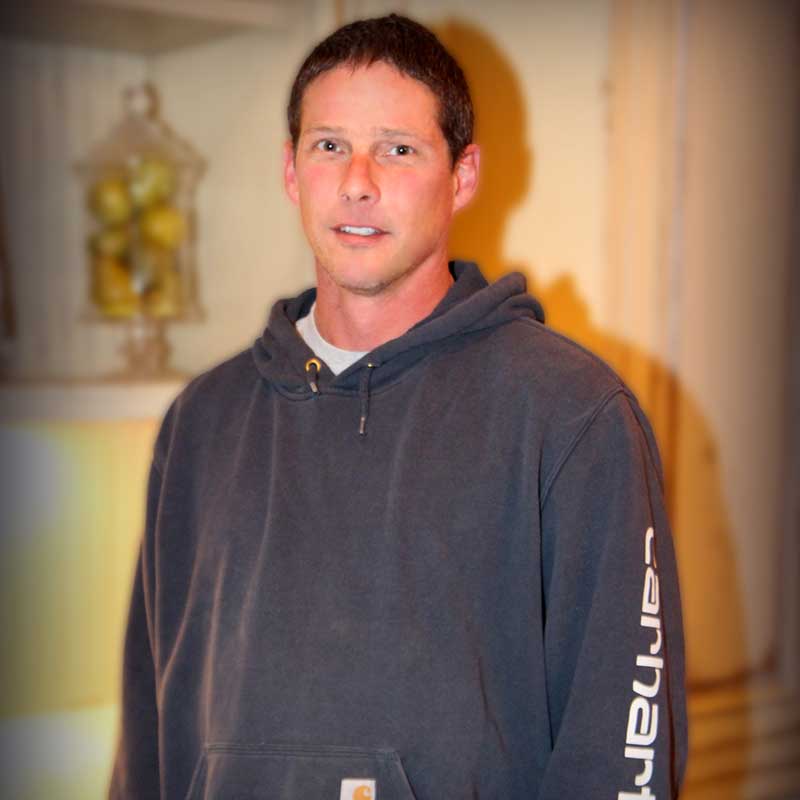 A man wearing a black hoodie standing in front of a wall.